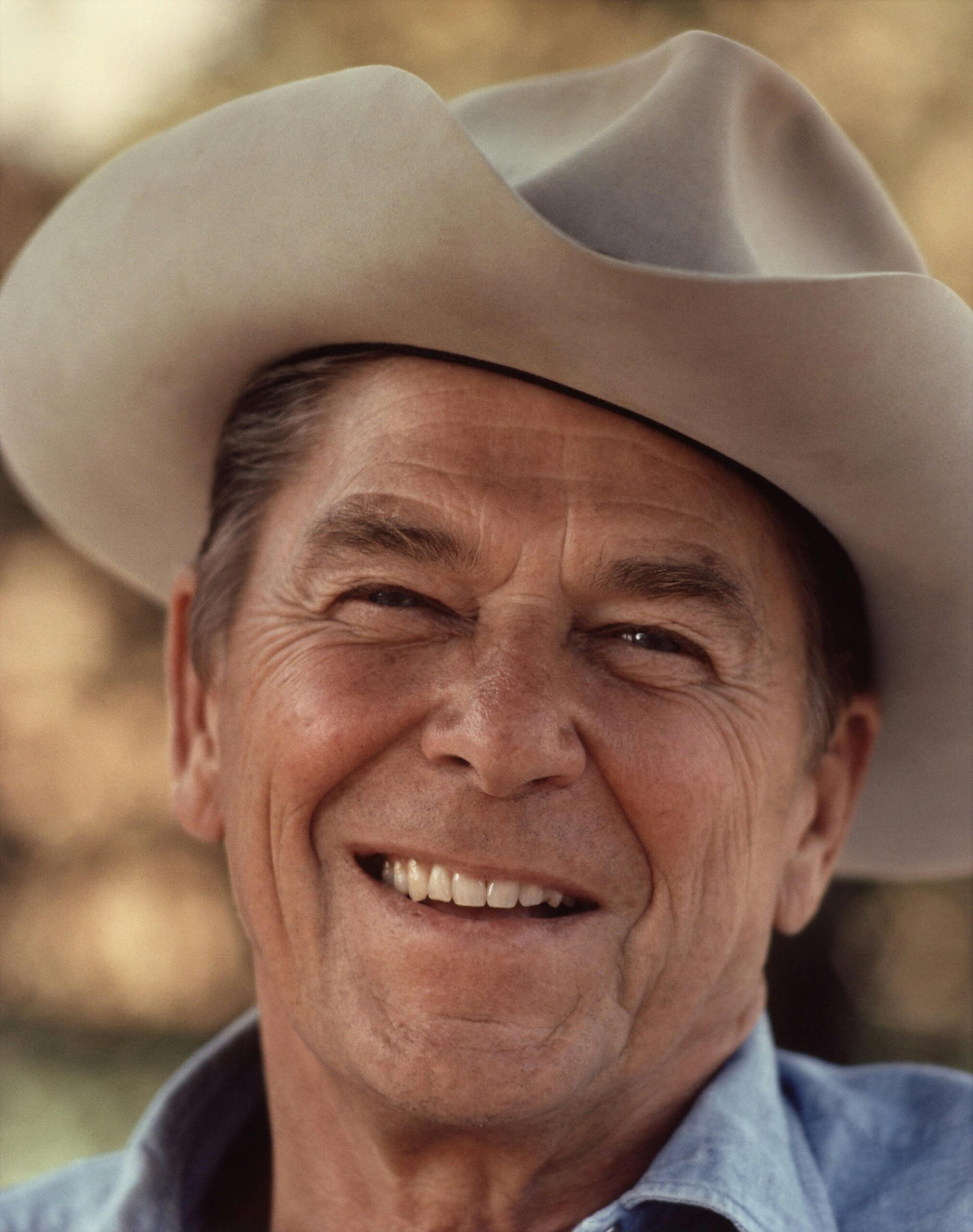 Portrait of a senior man wearing a cowboy hat, smiling warmly outdoors.