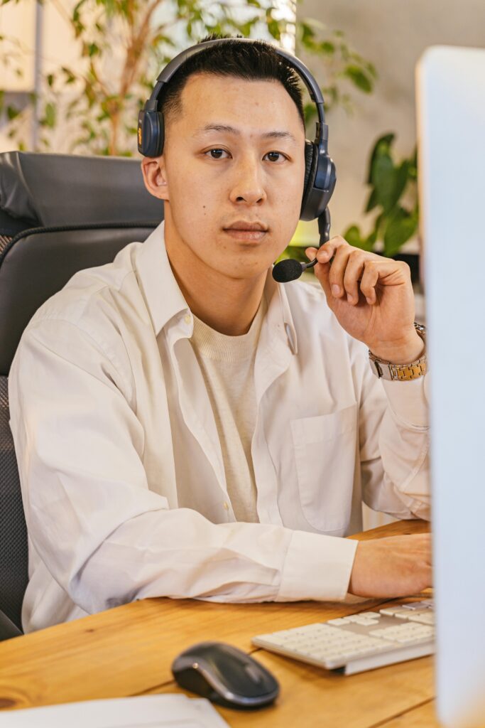 Asian man using a headset working at a desk in a modern office.